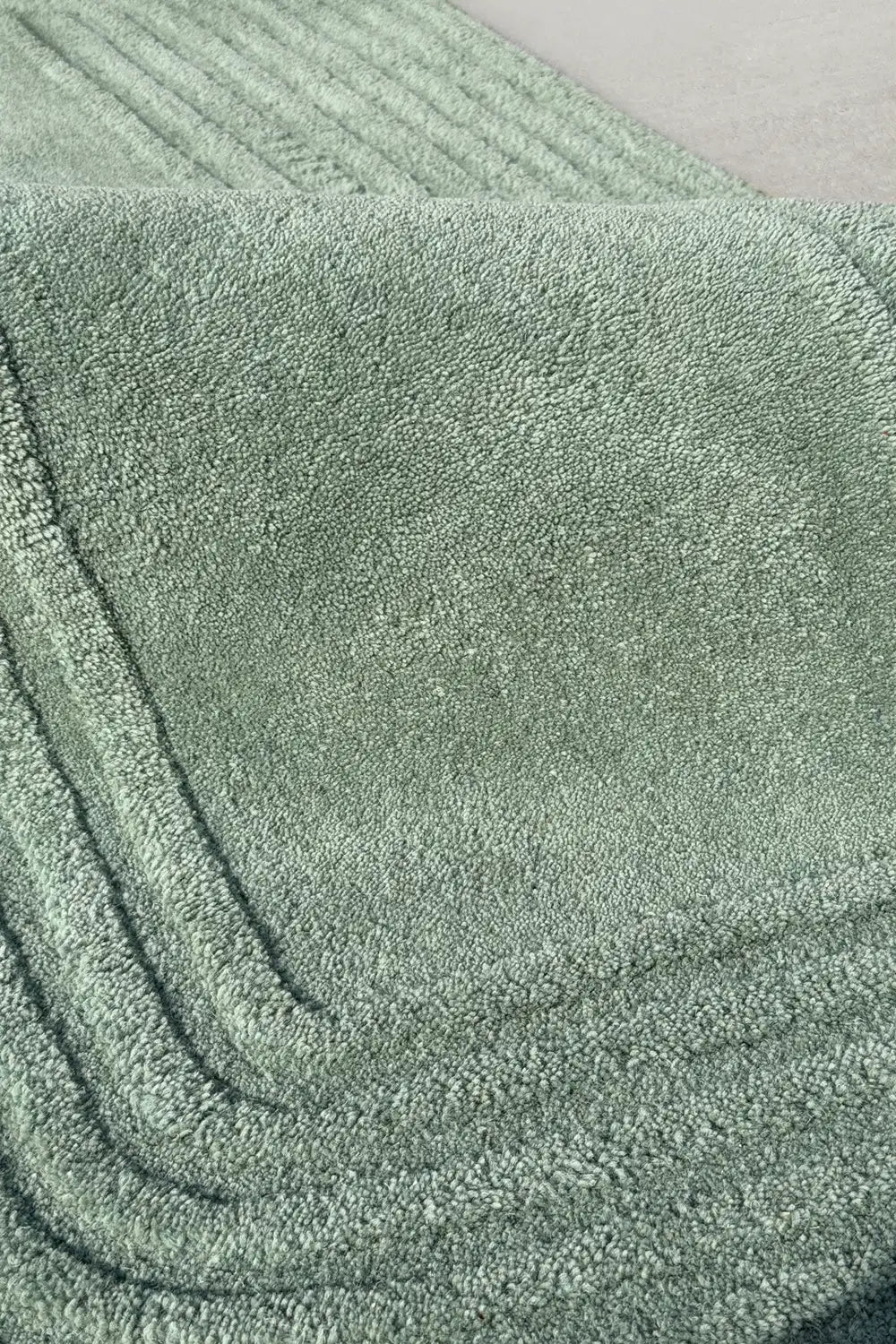 Close-up of plush wool carving on a sage green rug with a gentle curve, perfect for zen, japandi, or sustainable home decor