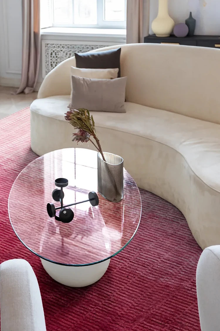 Modern living room with a curved beige sofa, glass coffee table, and red rug.