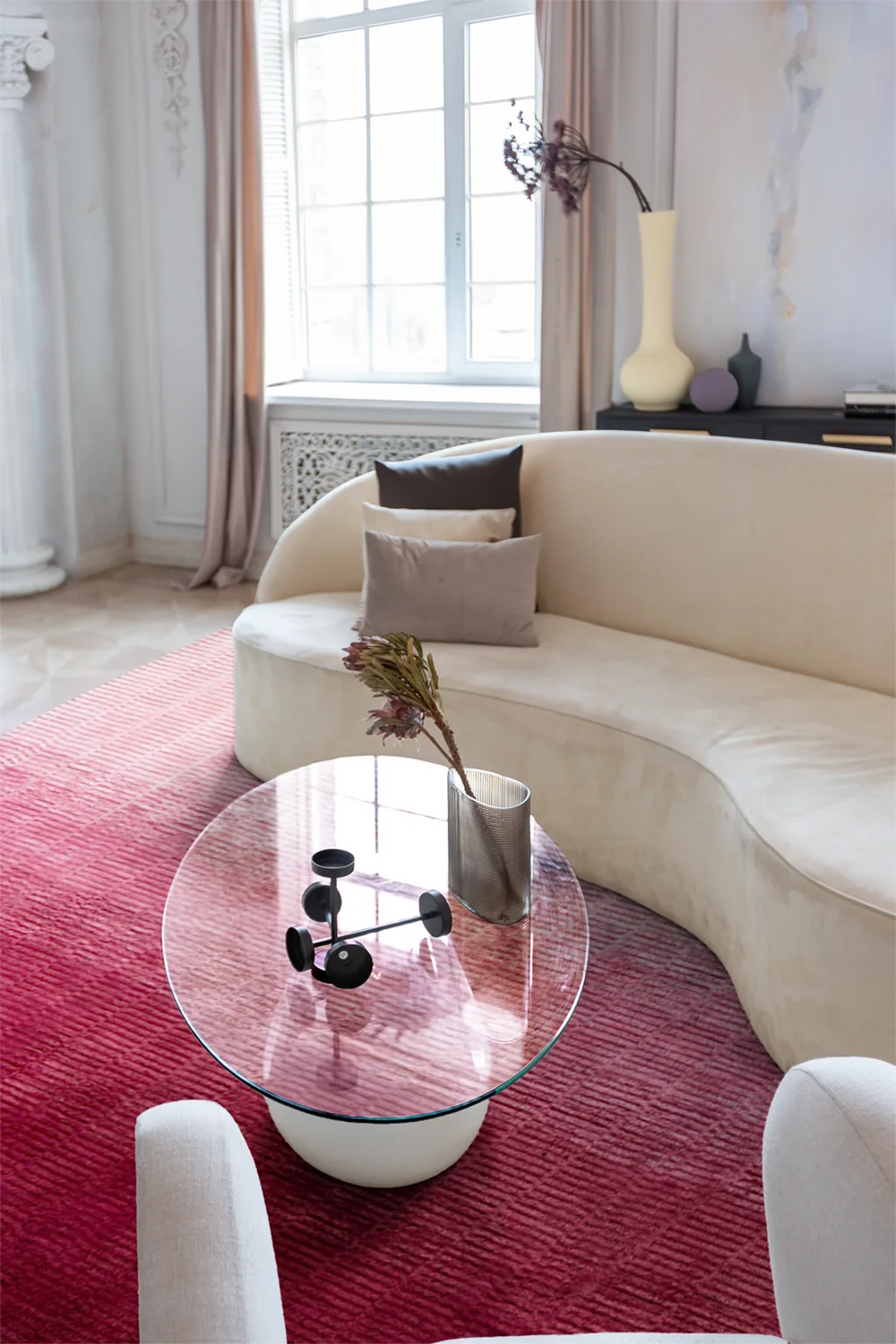 Modern living room with a curved beige sofa, glass coffee table, and pink rug.
