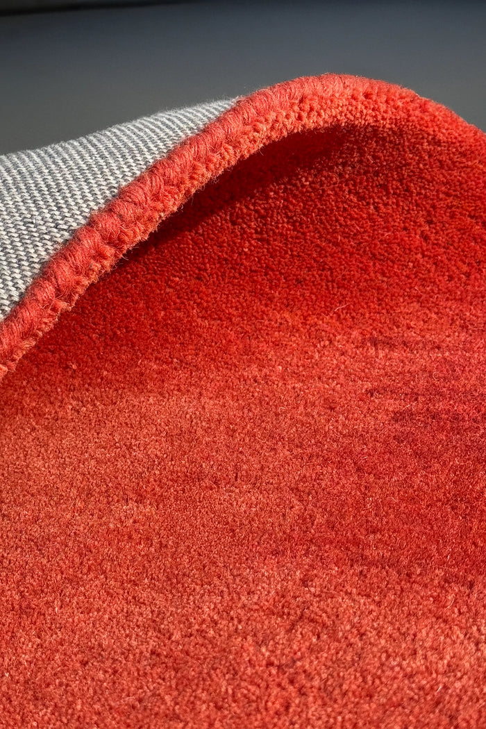 Close-up of a red textured rug or carpet with a tufted pile, showing the underside and a gray woven backing.