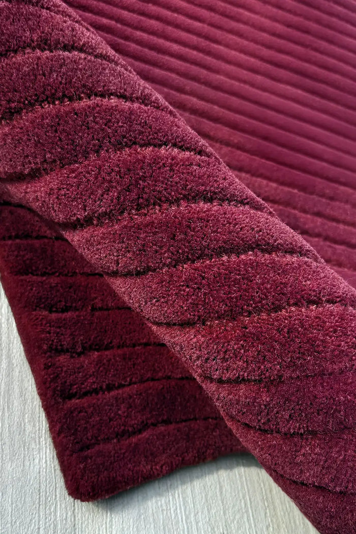 Close-up of a textured burgundy purple wool runner rug with a ribbed pattern on a light background.