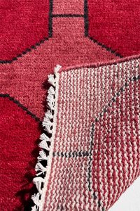 Close-up of a red and black geometric rug hand-knotted with white fringe