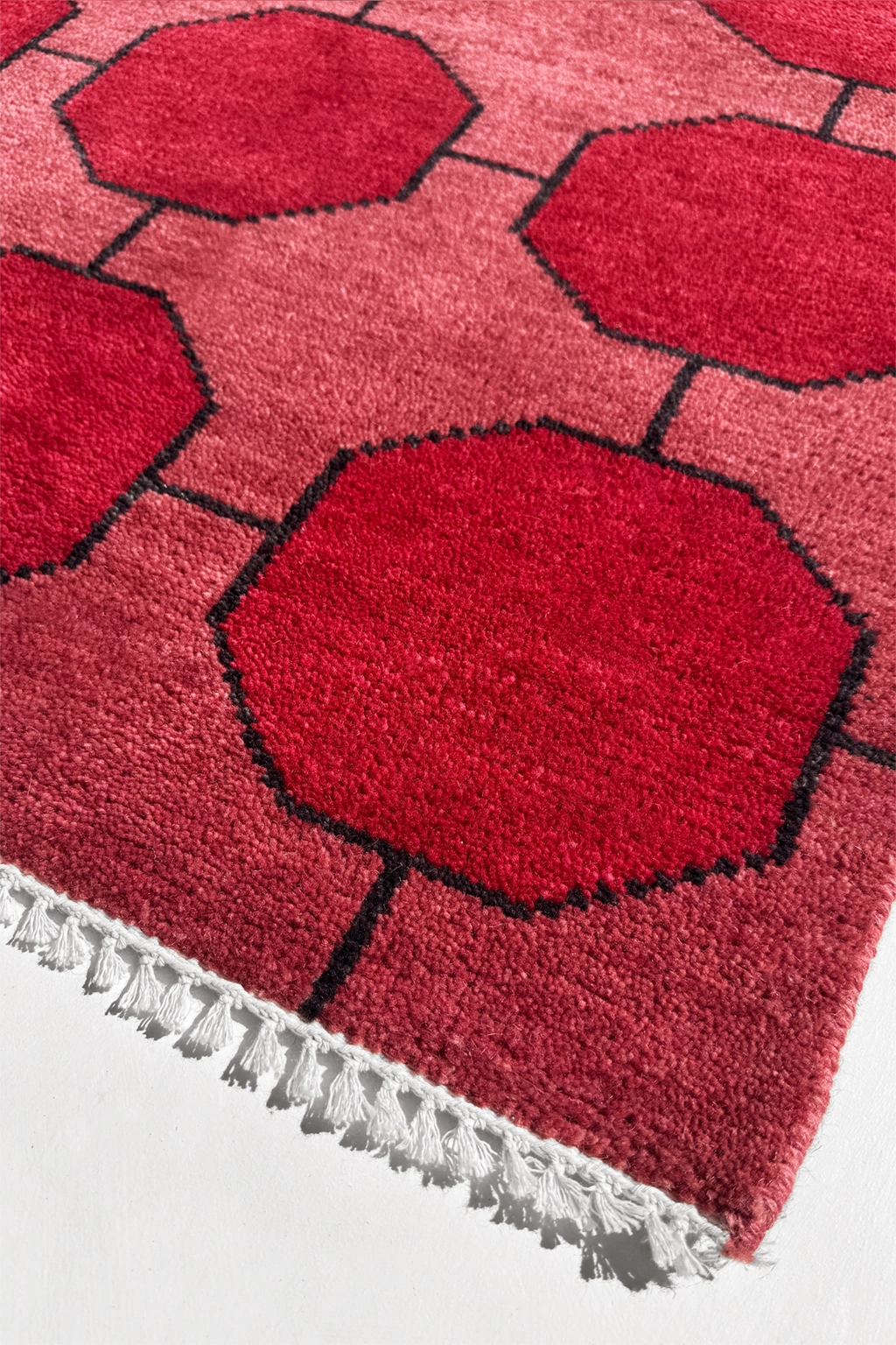 Red geometric patterned rug with white fringe on a white background