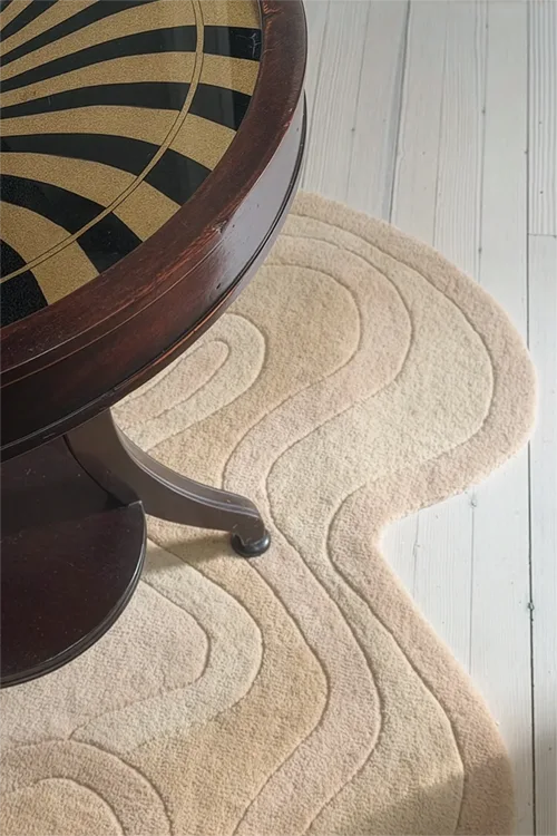 wavy beige textured rug on a light wooden floor with a wooden table corner.