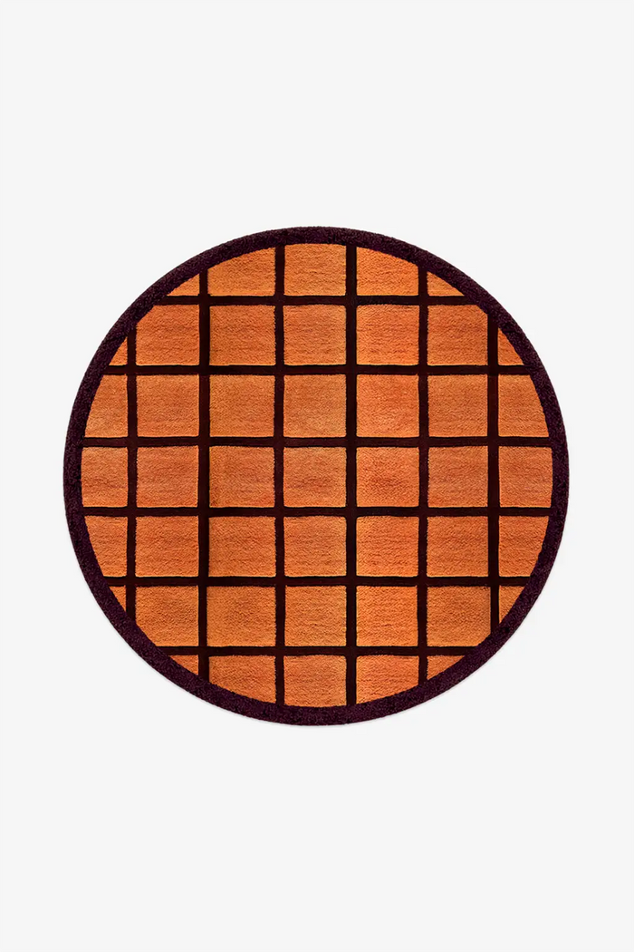 Round orange rug with burgundy grid pattern on a white background