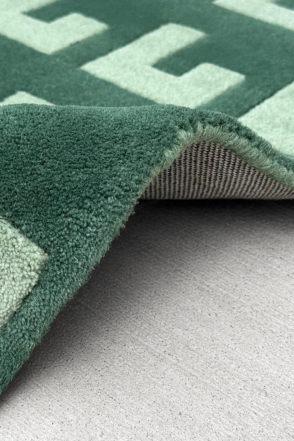 Close-up of a green geometric patterned runner rug on a gray surface