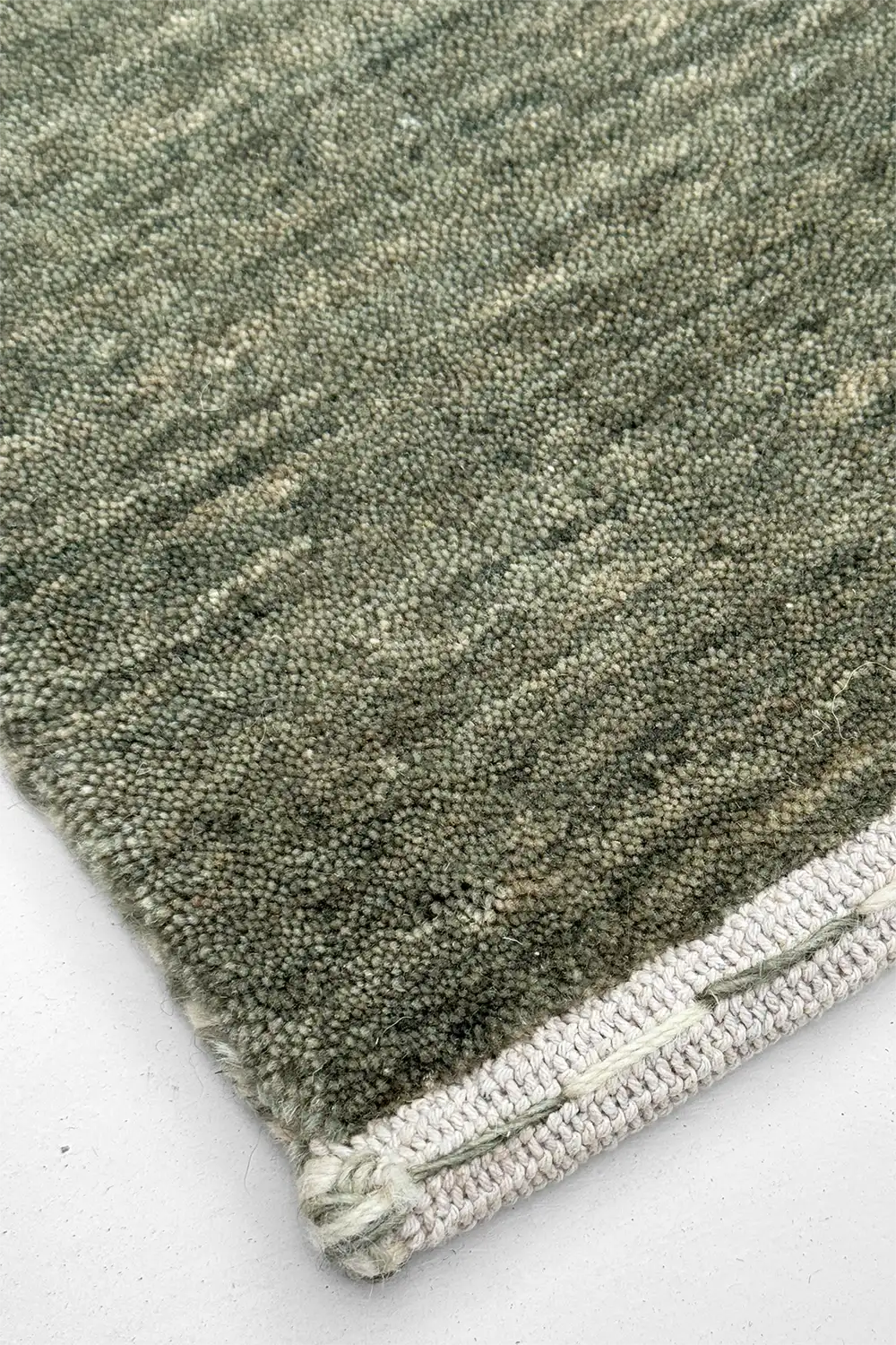 Close-up of a textured sage green rug corner on a white background
