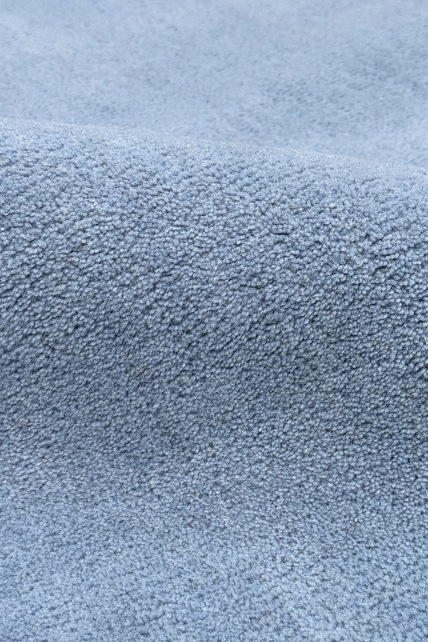 A close-up of a light blue textured wool rug, showing the fine woven material and soft folds.