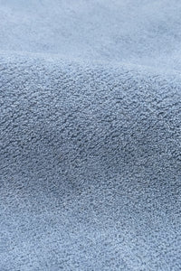 A close-up of a light blue textured wool rug, showing the fine woven material and soft folds.