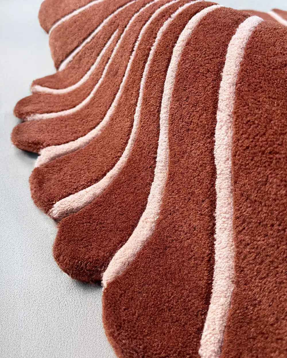 close-up texture of a unique sculpted wool rug with brown and cream carved stripes and scalloped edges, leaf shape rug