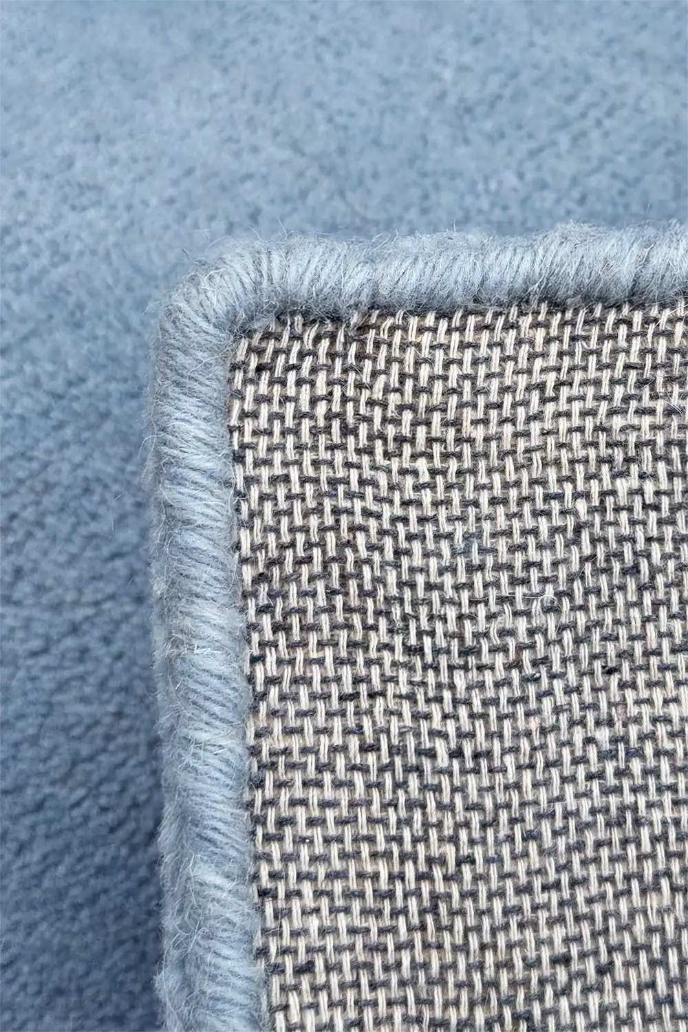 Close-up of a textured blue hand tufted wool rug with thick pile and hand serged binding