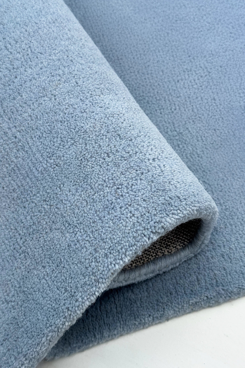 Close-up of a rolled-up square blue rug on a white surface