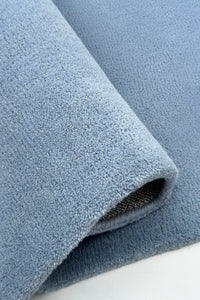 Close-up of a rolled-up square blue rug on a white surface