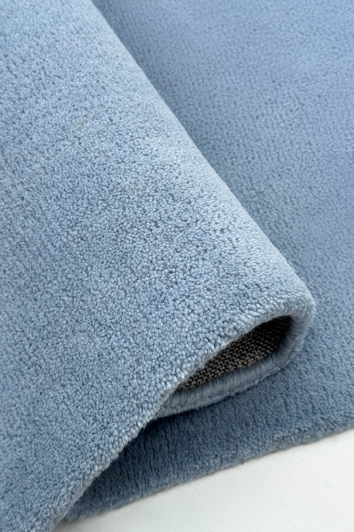Close-up of a rolled-up square blue rug on a white surface