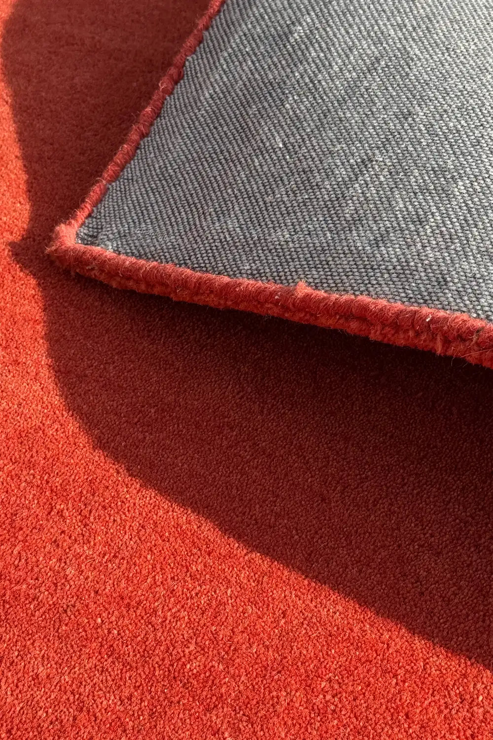 Close-up of red wool rug flipped at the corner to show durable backing