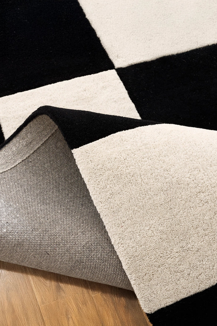 Close-up of a checkered patterned square rug with black, white, and gray texture colors on a wooden floor.