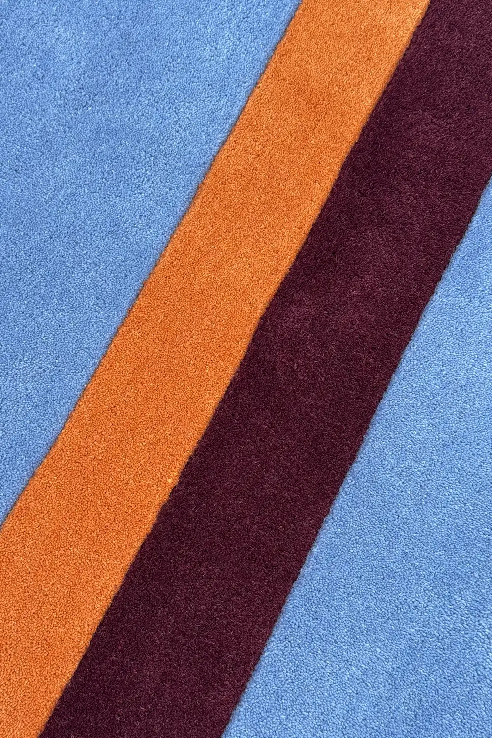Close-up of a rug with blue, orange, and burgundy stripes.