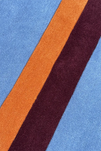 Close-up of a rug with blue, orange, and burgundy stripes.