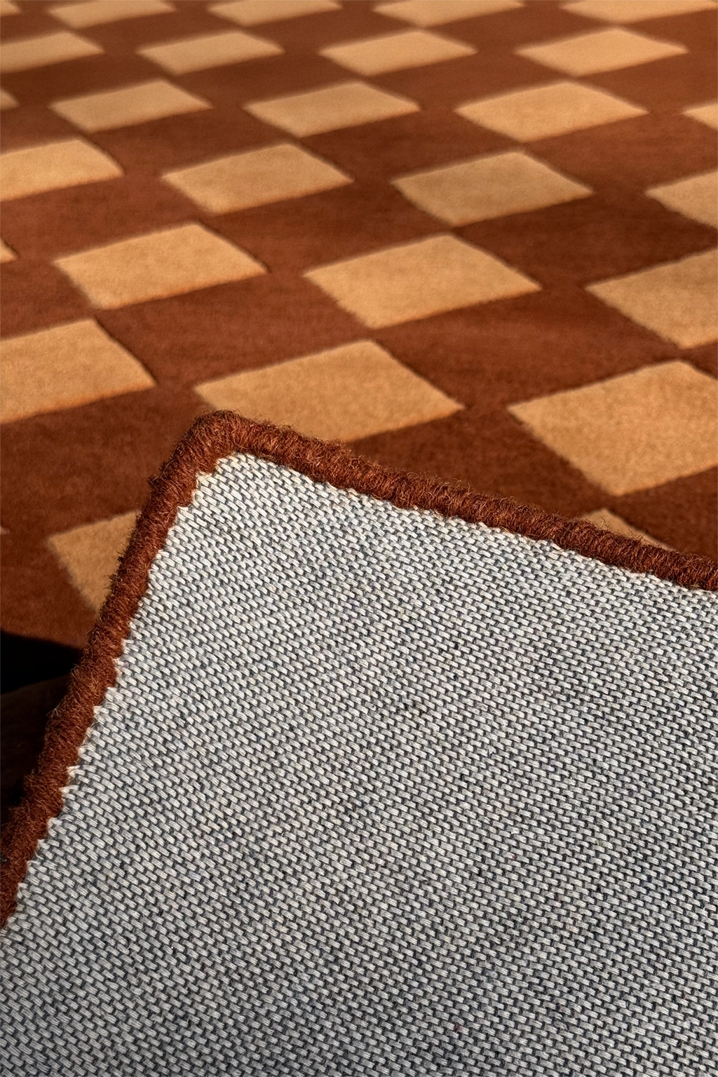 bound edge of a square brown wool rug with harlequin pattern
