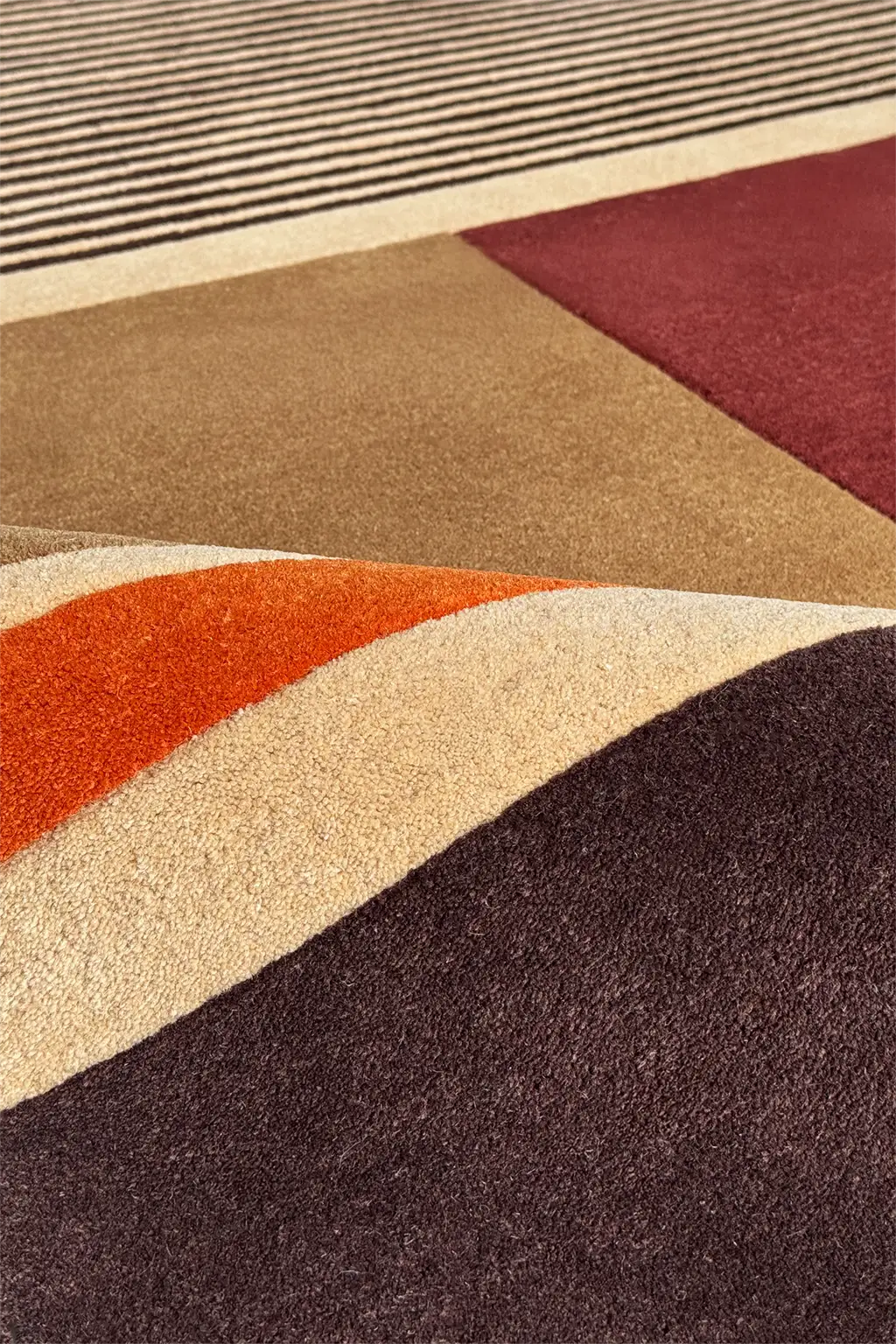 Close-up of a textured area rug with a modern geometric pattern featuring wavy and angular color blocks in dark brown, rust orange, cream, tan, burgundy, and black.