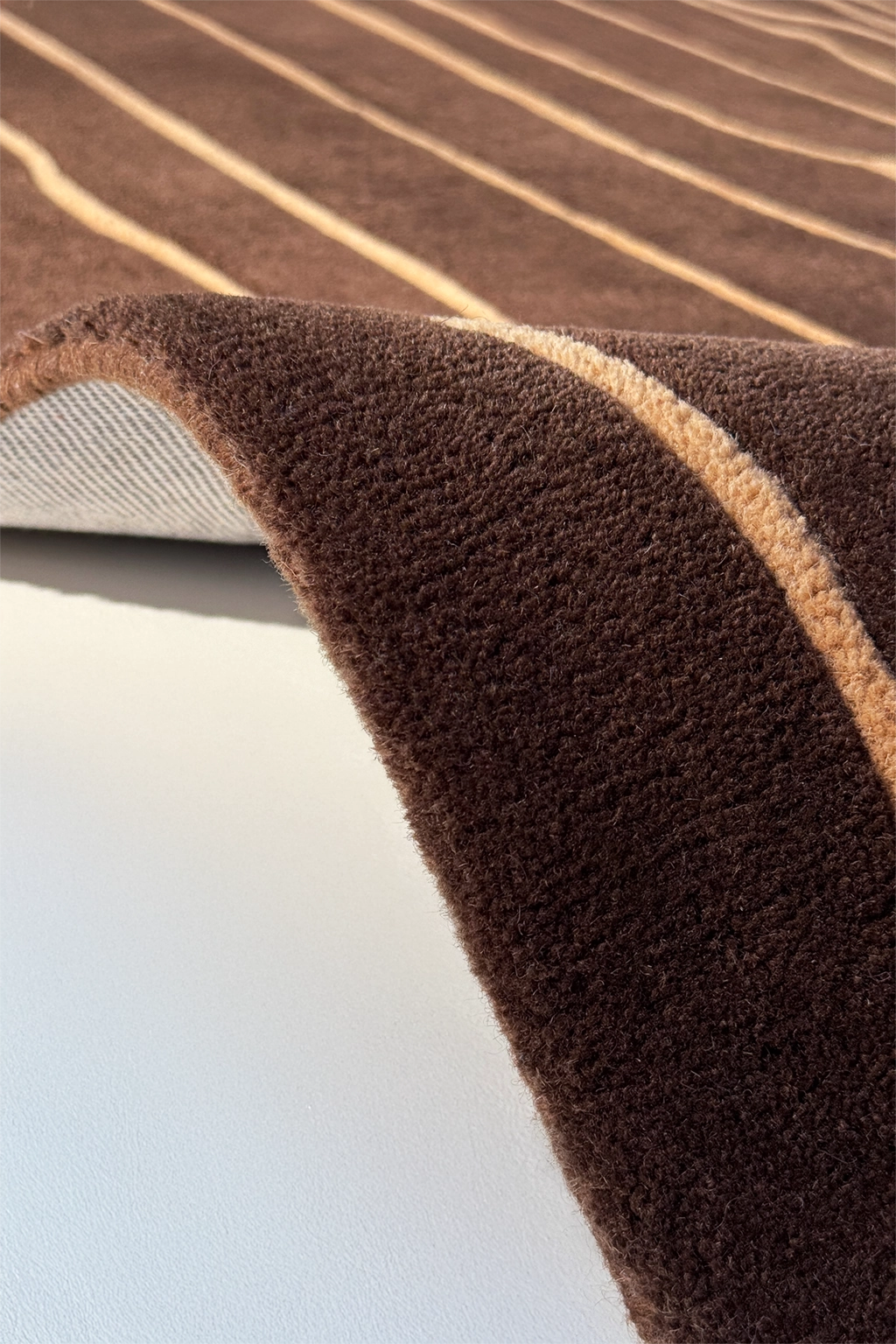 Close-up of a brown textured square rug with beige stripes on a white surface