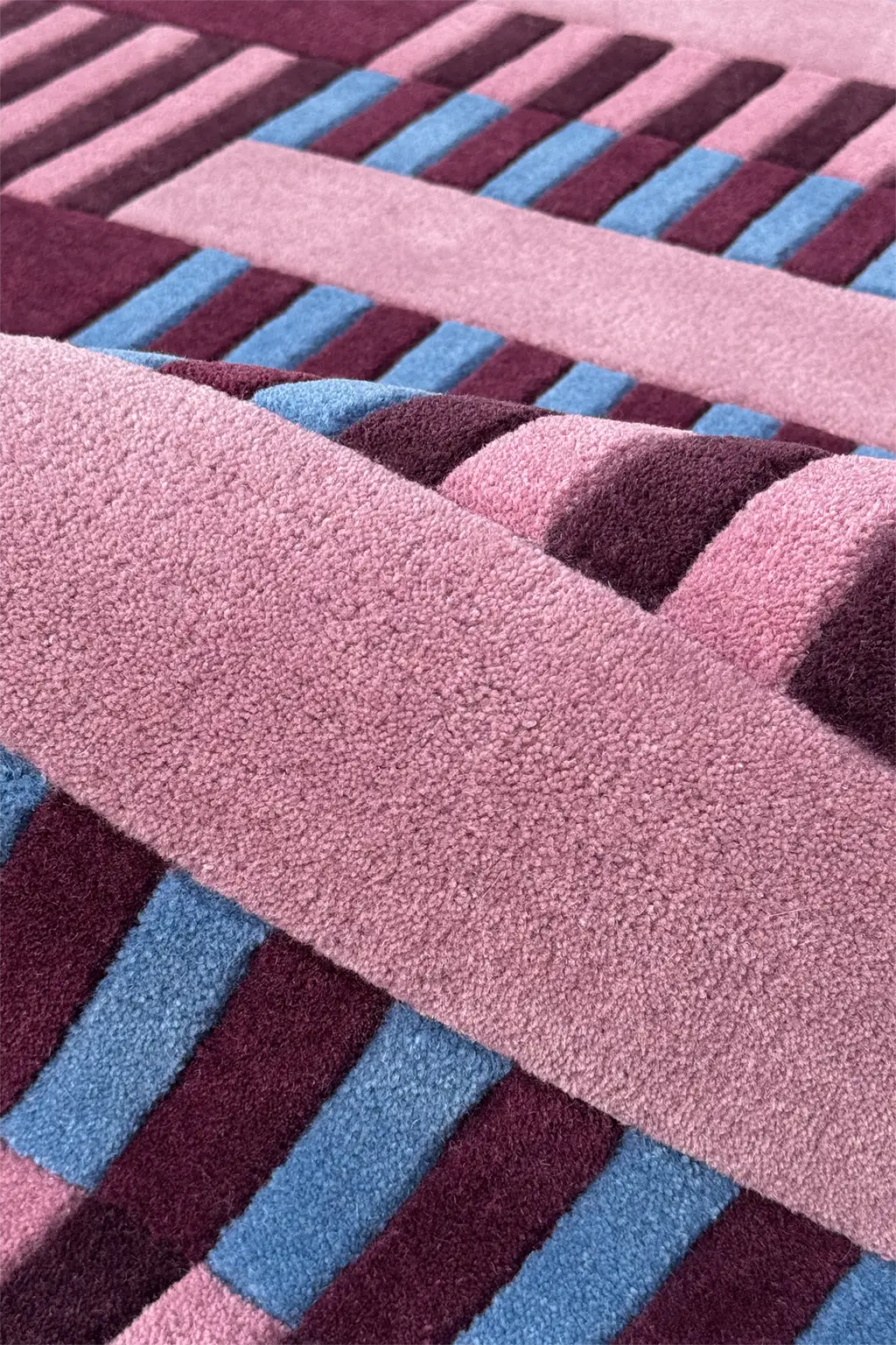 Close-up of a textured square rug with pink, blue, and purple stripes.