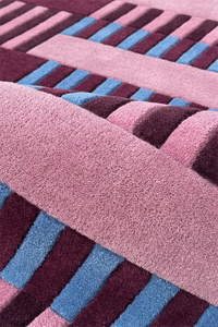 Close-up of a textured square rug with pink, blue, and purple stripes.