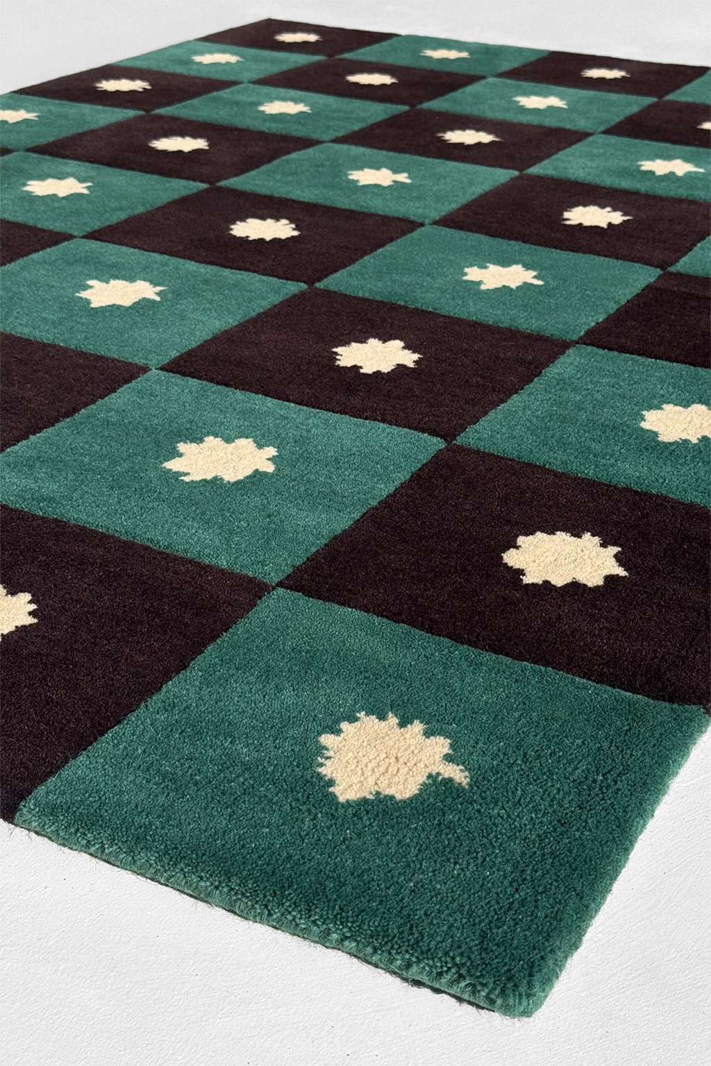 Checkered rug in black and green wool with star leaf patterns on a white background