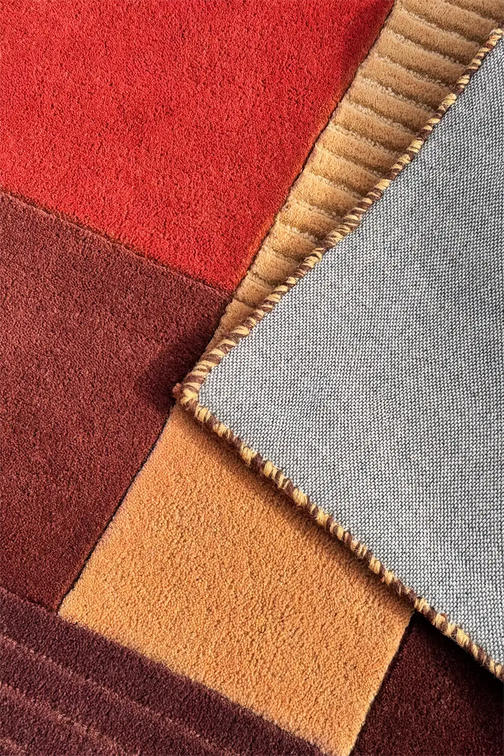 Close-up of a textured wool rug sample with red, brown, beige, and gold colors.