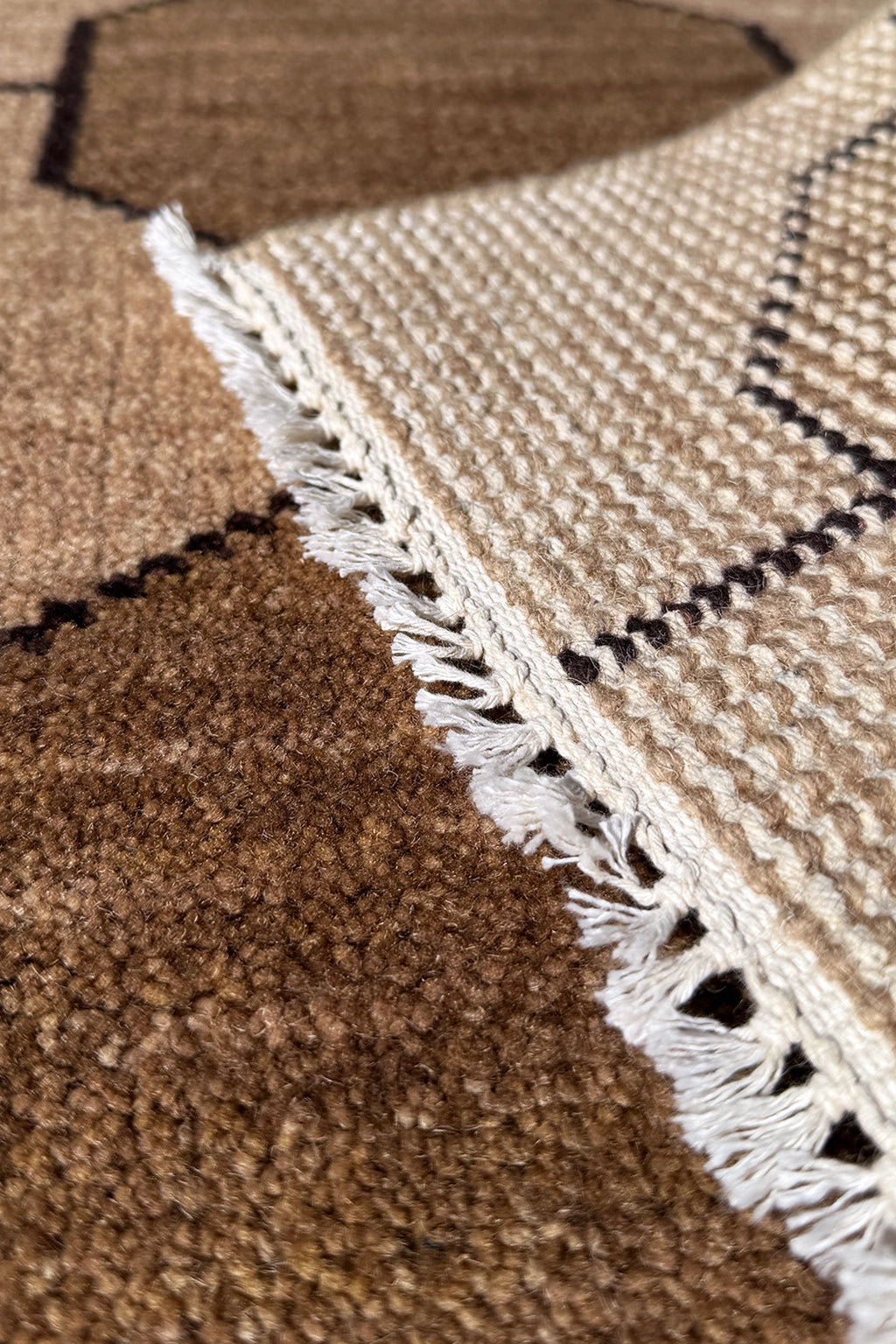Close-up of a textured taupe rug with a geometric pattern and white fringe.