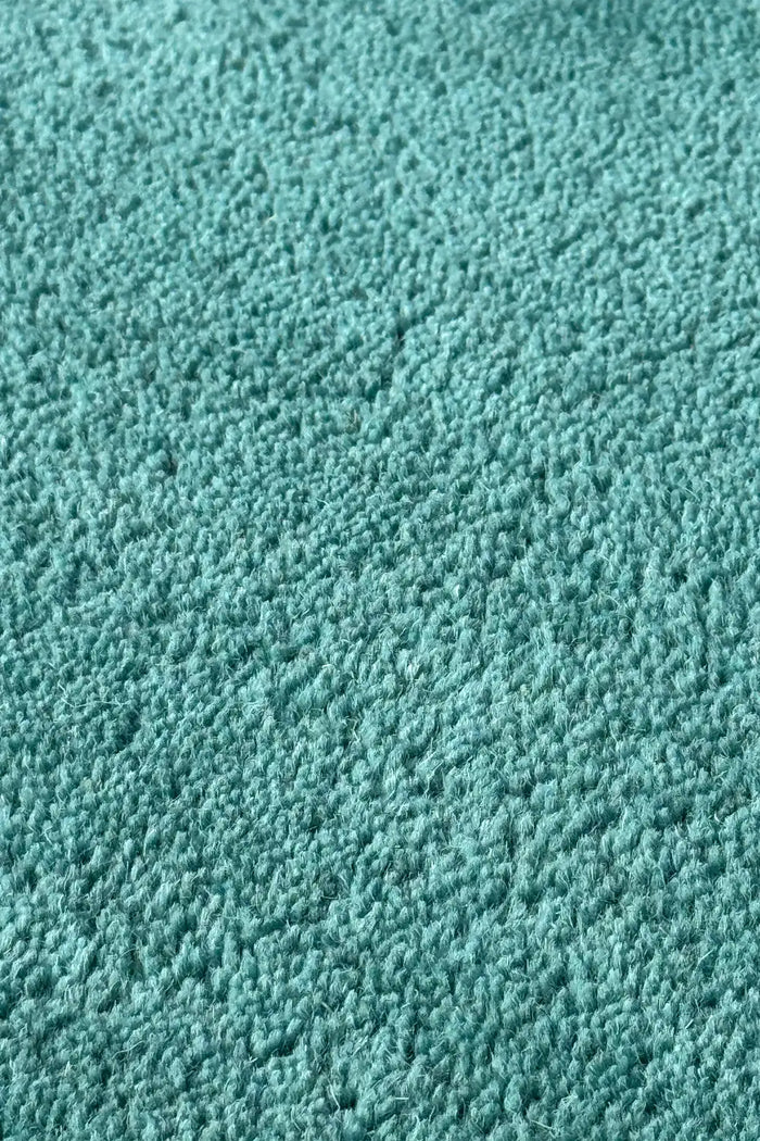 Zoomed-in texture of turquoise wool on a curved puddle rug, a vibrant option for funky area rugs or oval rugs for bedrooms teal