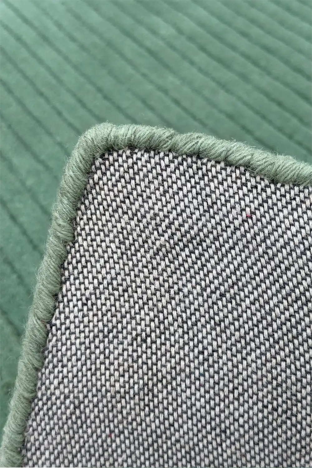 Close-up of a textured sage green tufted rug with a woven pattern