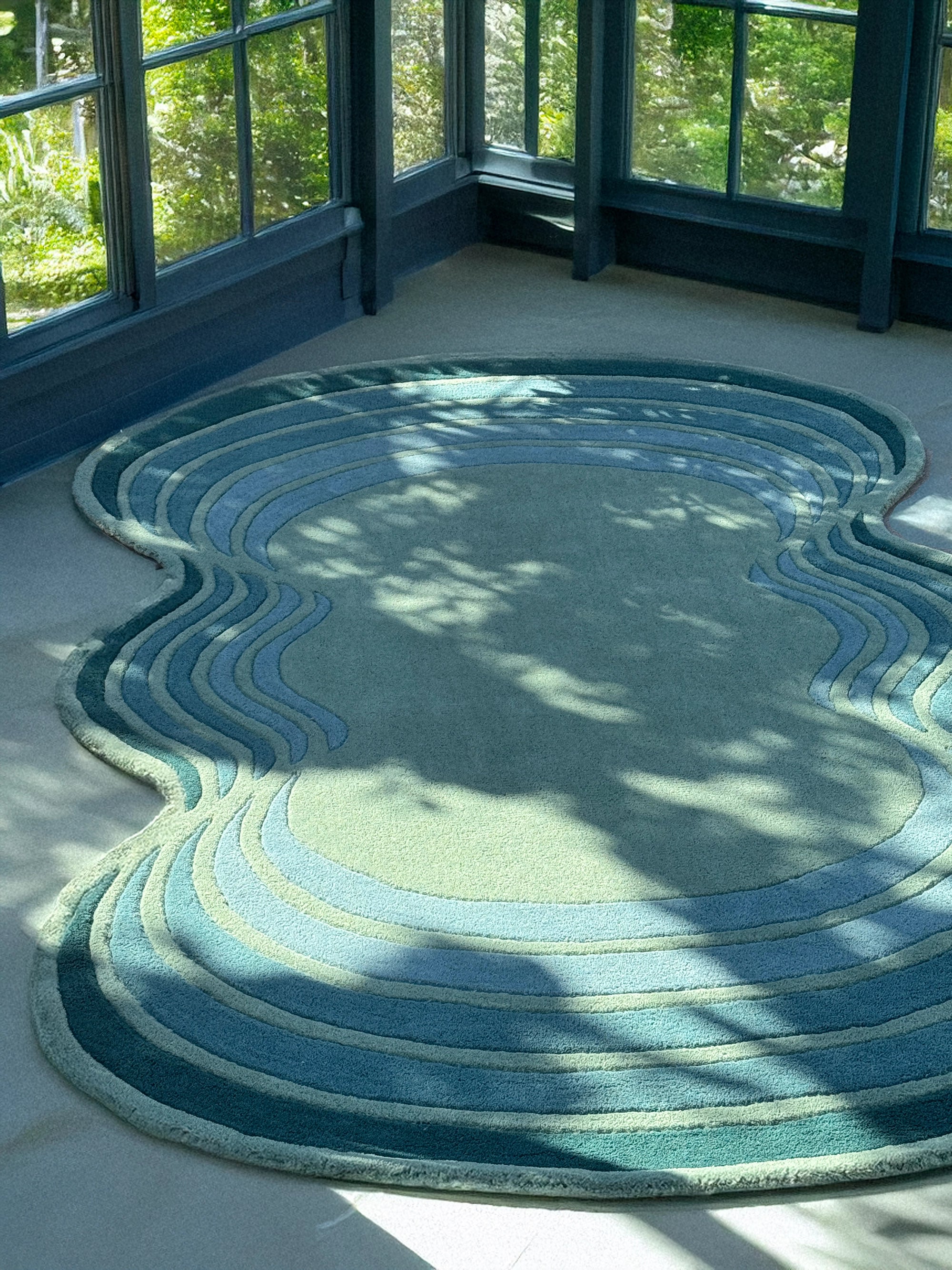 Rounded blue and green rug on a light-colored floor with large windows in the background.