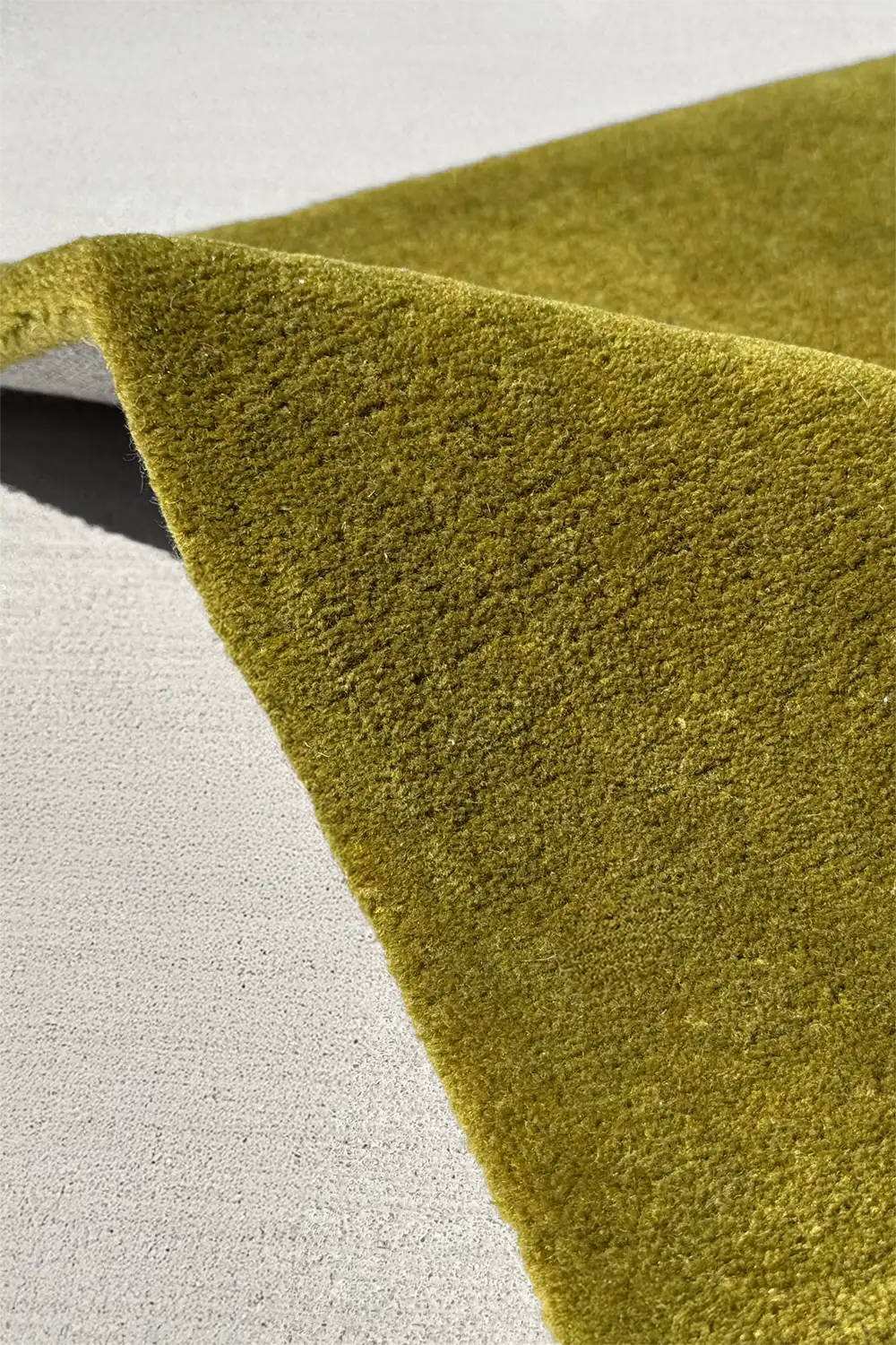 Close-up of a green textured tufted wool rug on a light gray background