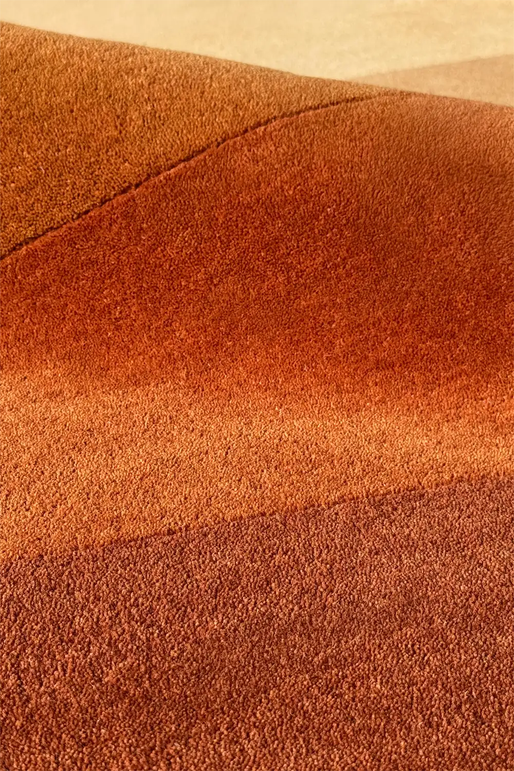 Sculpted wool rug with gradient shading in orange and brown, highlighting unique cutout shape