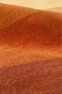 Sculpted wool rug with gradient shading in orange and brown, highlighting unique cutout shape