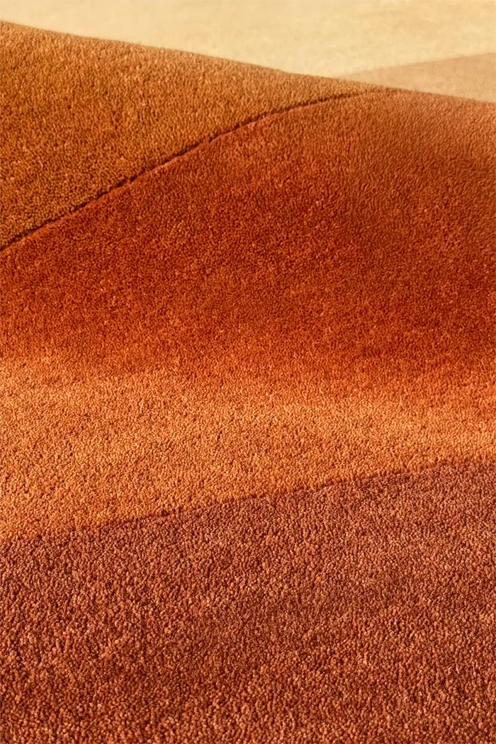 Sculpted wool rug with gradient shading in orange and brown, highlighting unique cutout shape