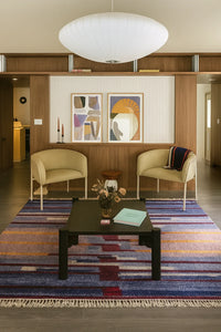 Living room with a multicolor striped modern rug two beige chairs, a coffee table, and abstract art on the wall lifestyle