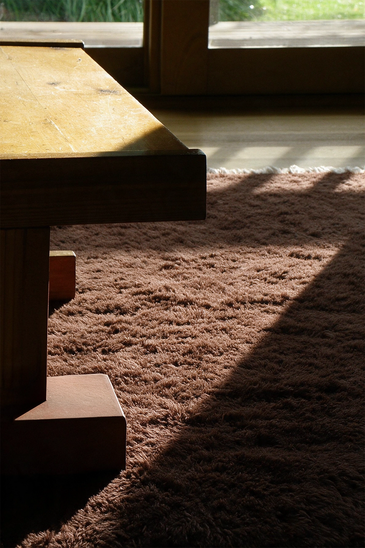 a sunny dining room with a large wooden block table on top of a shaggy brown wool area rug lifestyle