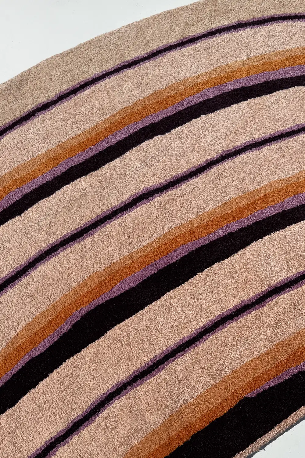 Close-up of a rug with brown, black, and purple stripes on a beige background lifestyle
