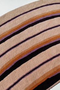 Close-up of a rug with brown, black, and purple stripes on a beige background lifestyle