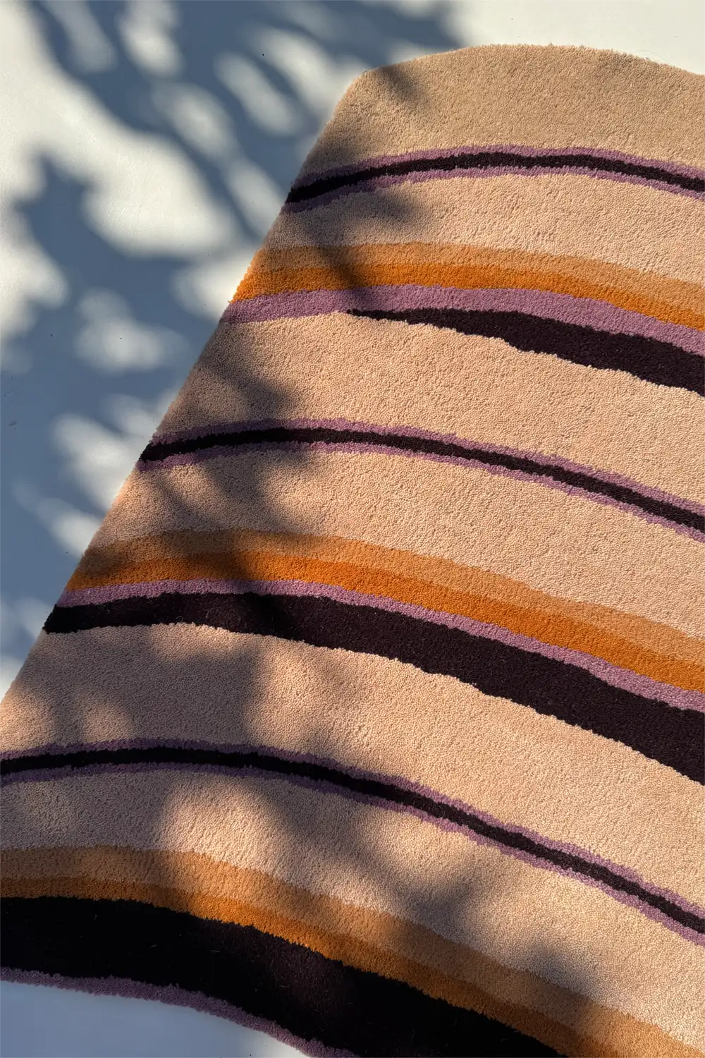 Close-up of a striped rug with brown, orange, and purple colors on a light background lifestyle