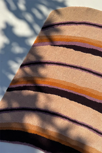 Close-up of a striped rug with brown, orange, and purple colors on a light background lifestyle