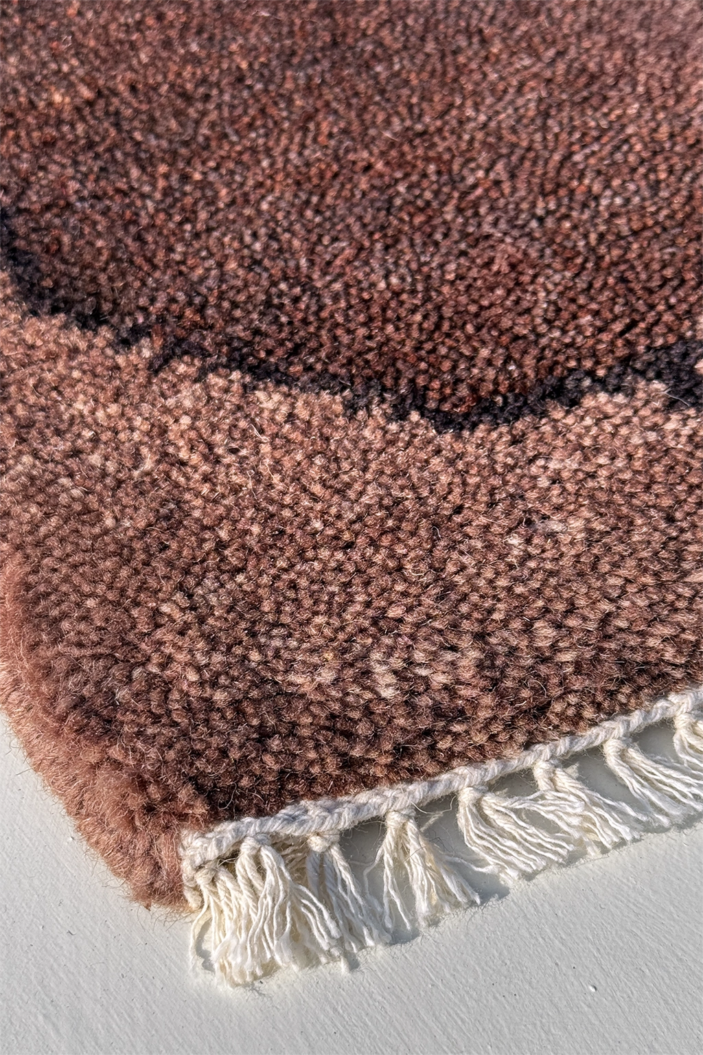 dark walnut textured rug with white fringe on a light gray background