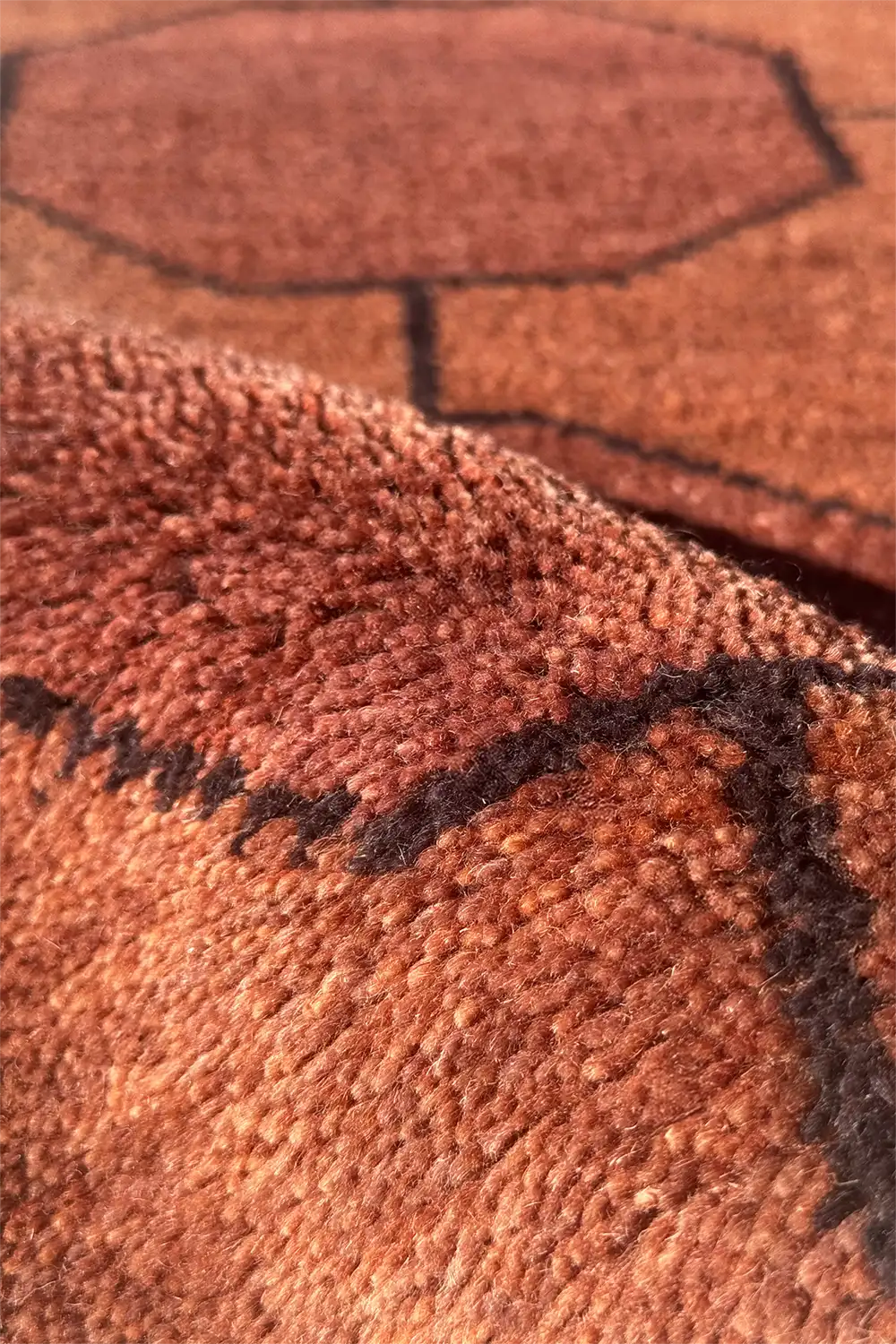 Close-up of a textured reddish brown rug with geometric pattern hand-knotted in premium wool
