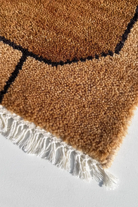honey gold textured rug with black geometric pattern and white fringe on a light gray background