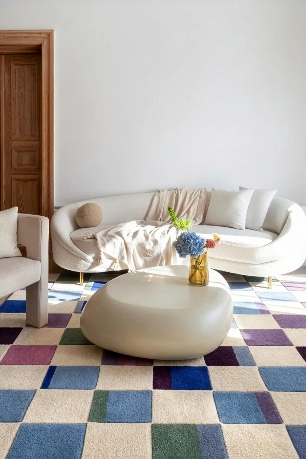 Modern living room with a colorful checkered rug, white sofa, and a small table with flowers lifestyle