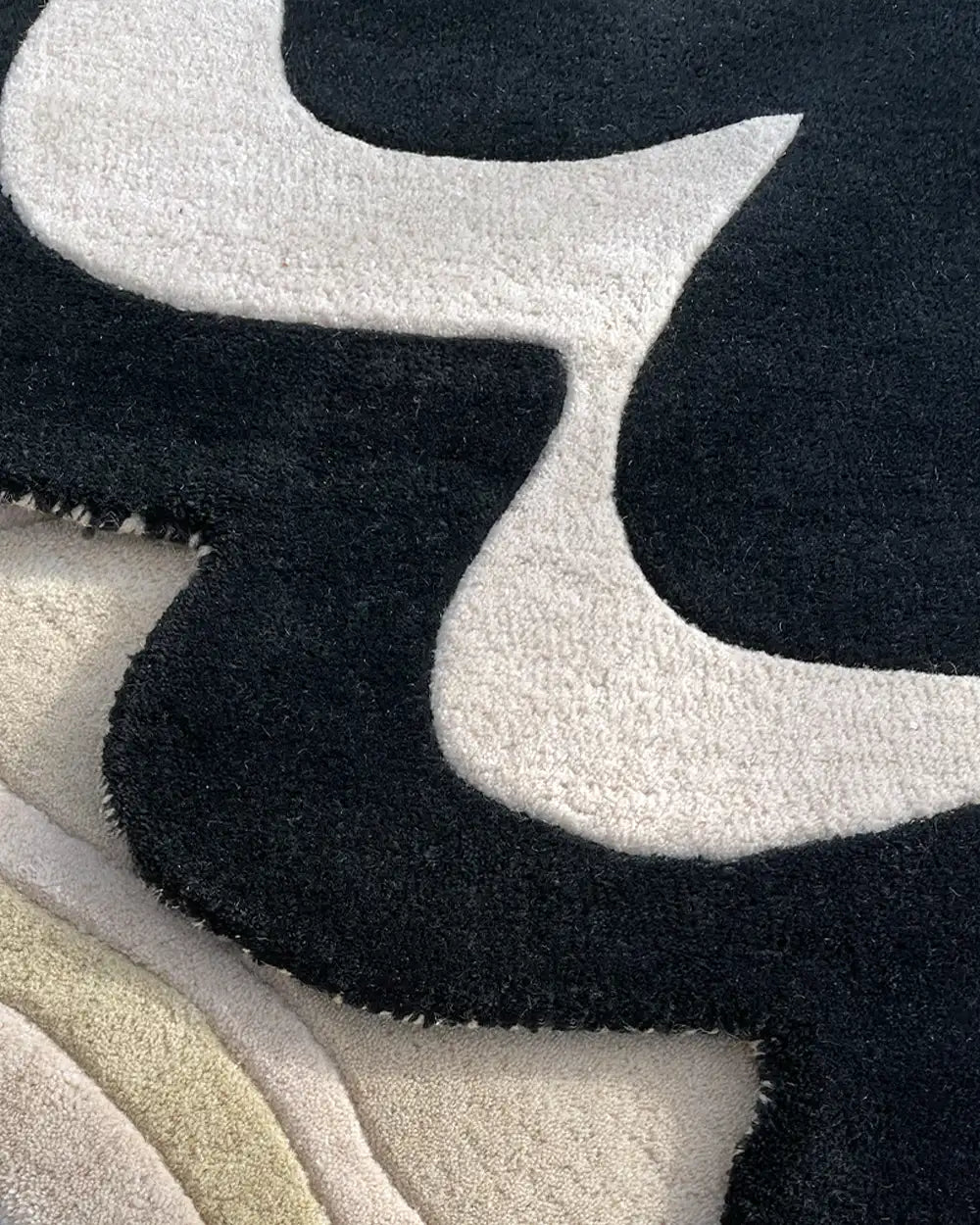 close up texture of two irregular shaped wool rugs, one with a graphic black and white pattern and one underneath with neutral tones