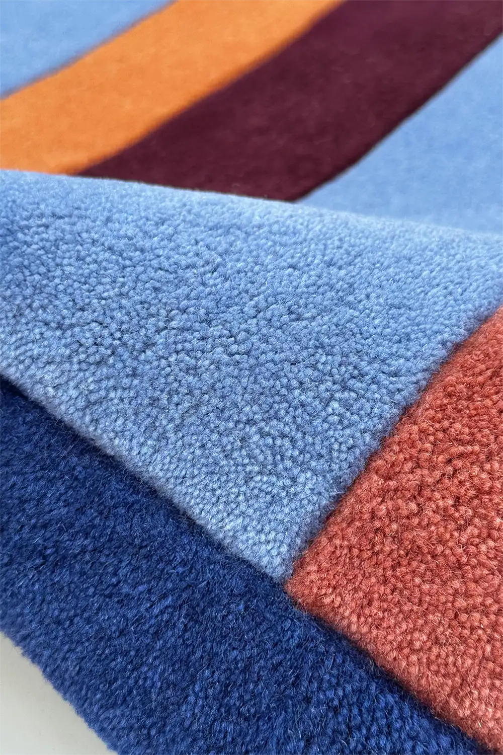 Close-up of a multicolored textured tufted wool rug with shades of blue, orange, red, and purple.
