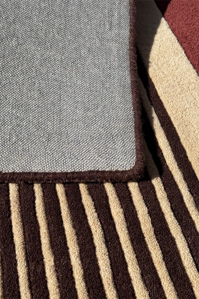 Close-up of a textured runner rug showing a gray top section with a dark brown border, layered over a brown and beige striped section.